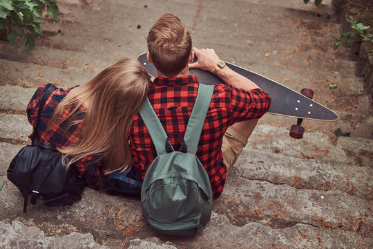 Back view of a young hipster couple, sitting on steps in a park.