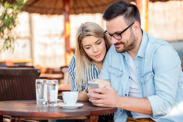 Happy young couple smiling and browsing internet on a smart phone in a cafe