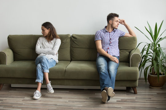 Husband and wife sitting on different sides of couch not looking at each other and not talking, being in quarrel thinking about relationship problems, break up. Concept of family misunderstanding