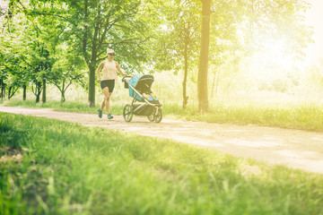Running woman with baby stroller enjoying summer in park