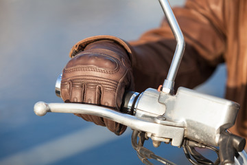 Naklejka premium Ramię motocyklisty w brązowej skórzanej rękawiczce posiada przepustnicę obrotowego uchwytu, widok z bliska