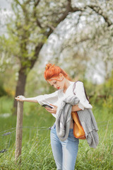 Beautiful young woman walking outside in a field, looking at her cell phone, sunny, rural mood 