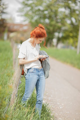 Beautiful young woman walking outside in a field, looking at her cell phone, sunny, rural mood 