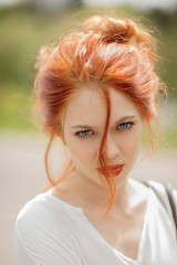 beautiful young woman with red hair, outside in a park in the sunlight, looking into the camera, lifestyle concept shoot