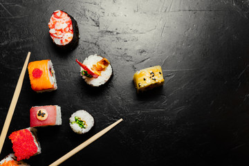Top view of Japanese Sushi and chopsticks on black background. Sushi rolls, nigiri, maki, pickled ginger, soy sauce. Space for text. Top view. Sushi background.