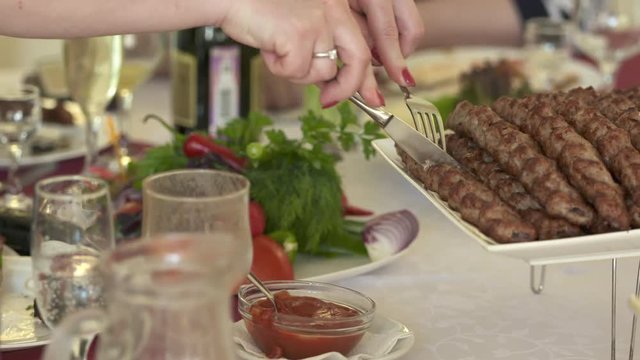 Armenian lula kebab served with chopped onion on decorative platter. People enjoying meal at festive dinner table in restaurant.