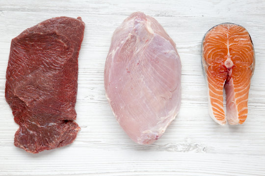 Uncooked Raw Beef Meat, Turkey Breast And Salmon Steak On White Wooden Background, Top View. Flat Lay. Closeup.