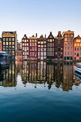 Fotobehang Amsterdam Uitzicht op kleurrijke gevels van typische Amsterdamse huizen die tijdens zonsondergang in het Amstelkanaal in Amsterdam reflecteren