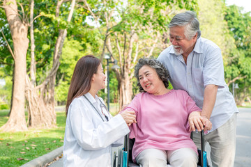 Nurse with senior patient in park. Senior disable woman in wheelchair relaxing and being comfort by a chinese female nurse.