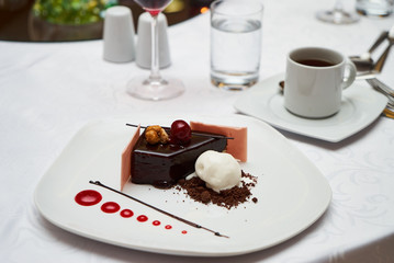 Black forest Cake with cherry, vanilla ice-cream, chocolate and cup of hot tea on table. Delicious sweet dessert breakfast on table background, close-up