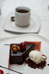 Black forest Cake with cherry, vanilla ice-cream, chocolate and cup of hot tea on table. Delicious sweet dessert breakfast on table background, close-up
