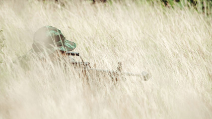Soldier hiding in bushes ready to shoot. Ambush his ememy, ready his assault rifle. Hiding below the tree line. Military combat training concept.