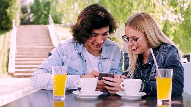Young couple sitting in cafe's garden and using smartphone for fun