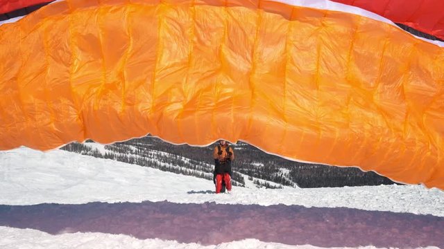 raises the sail wing of the paraglider. He starts to take off, breaks away from the ground, runs away. Paragliding in winter. Slow motion