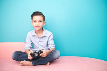 Obraz premium Young boy isolated in blue. Handsome early teenage boy portrait. Playing game console with joy pad. Technology concept.