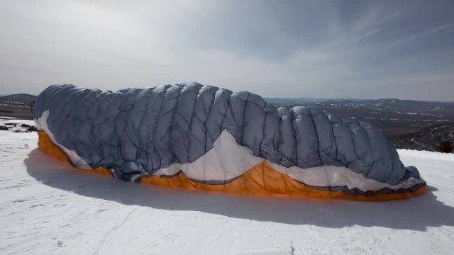 raises the sail wing of the paraglider. He starts to take off, breaks away from the ground, runs away. Paragliding in winter. Slow motion