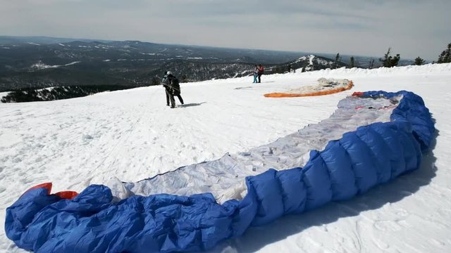 raises the sail wing of the paraglider. He starts to take off, breaks away from the ground, runs away. Paragliding in winter