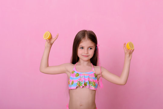 Caucasian beautiful little girl with fresh yellow lemons on a pink background
