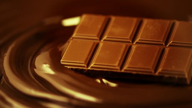 Chocolate bar rotated over melted dark chocolate swirl liquid background. Confectionery concept backdrop. Sweet dessert. Slow motion 4K UHD video 3840X2160