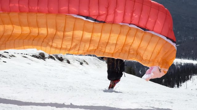 raises the sail wing of the paraglider. He starts to take off, breaks away from the ground, runs away. Paragliding in winter. Slow motion