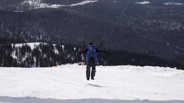 raises the sail wing of the paraglider. He starts to take off, breaks away from the ground, runs away. Paragliding in winter