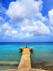 beautiful view of the sea in bonaire with a deck or harbor blue sky and clouds and some boats