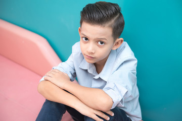 Young boy on pink sofa. Handsome early teenage boy portrait. Cool looking pose.