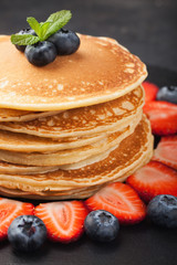 Delicious pancakes close up, with fresh blueberries, strawberries on a black stone background