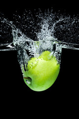 close up view of green apple falling into water isolated on black