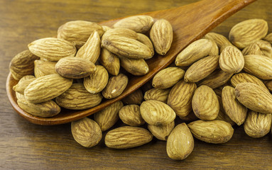 Almonds seeds pour from wood spoon on textured wooden background, top view.