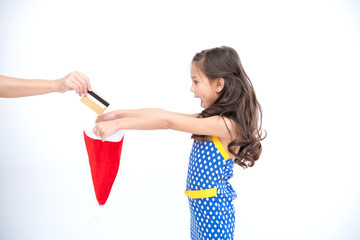 Young girl got money for christmas present. Young cute white girl holding a santa hat while her mother dropping gold credit card into the hat, surprise her. Family christmas concept.