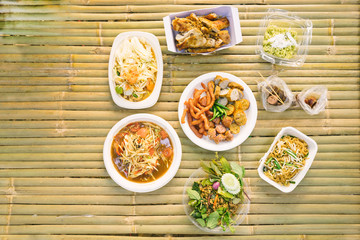 Top view of local Thai food such as Som Tum - Spicy papaya salad, Chicken grill, Pad Thai, Num Tok - Grilled pork on the wooden table.