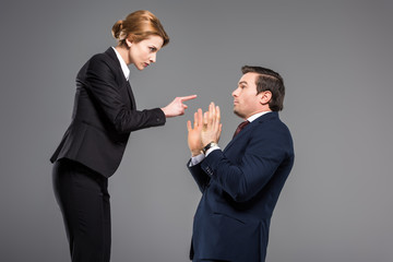 angry businesswoman quarreling and pointing at scared businessman, isolated on grey