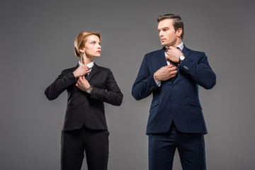 serious businesswoman and businessman fixing ties and looking at each other, isolated on grey, feminism concept