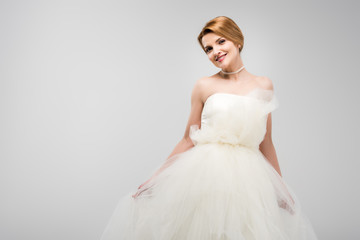 Fototapeta na wymiar beautiful smiling bride posing in white wedding dress, isolated on grey