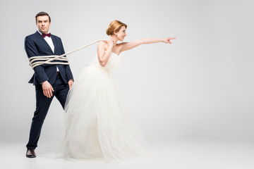 bride pointing and pulling groom bound with rope, isolated on grey, feminism concept