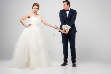 attractive bride in wedding dress and groom bound with rope, isolated on grey, feminism concept