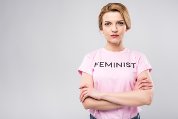 confident woman in pink feminist t-shirt with crossed arms, isolated on grey