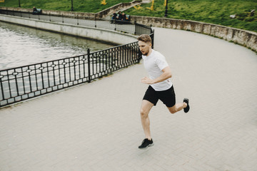 Healthy blonde man running in the morning around the lake while measures his heart beats.