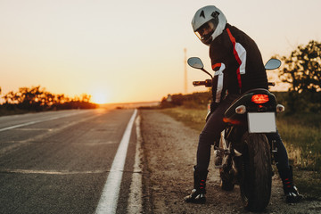 Back view of a amazing man sitting on his bike equipped for reading and traveling looking into camera against sunset.