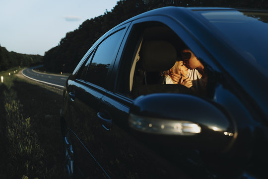 Beautiful caucasian couple stopped near the road in the car in forest to admire direct light of sunset. Amazing young couple traveling with the car in their vacation time.