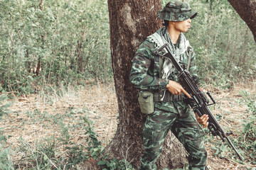Soldier standing behind a tree ready to attack. Chinese male soldier standing behind a large tree...