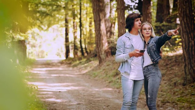 Young Couple Using Smartphone While Walks Through Forest