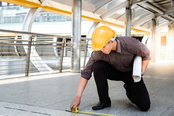 Handsome asian worker or engineer man is measuring the floor by using tape line or tape measure for doing his work. A guy wears hard hat and holds blueprint. A man is working and solving some problem
