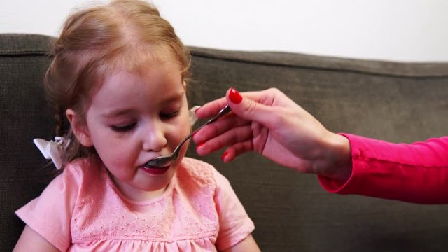 A little girl can't take her eyes off her smartphone while she's being fed