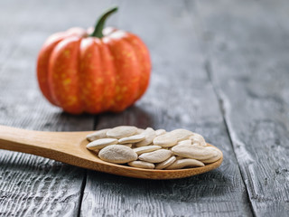 Wooden spoon with pumpkin seeds and pumpkin fruits on black rustic table.