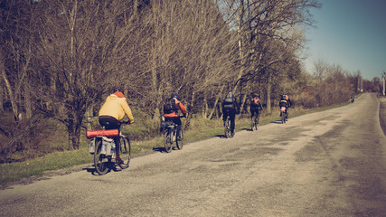 Fototapeta premium Group of young people riding bicycles on countryside road, image with warm vintage toning