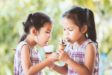 Obraz premium Two asian little child girls eating delicious icecream waffle cone together with fun and happiness