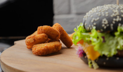 Black burger on a wooden background with potatoes and sauce