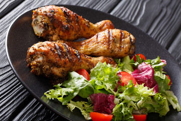 Barbecue serving of grilled chicken drumsticks and fresh vegetable salad closeup. horizontal